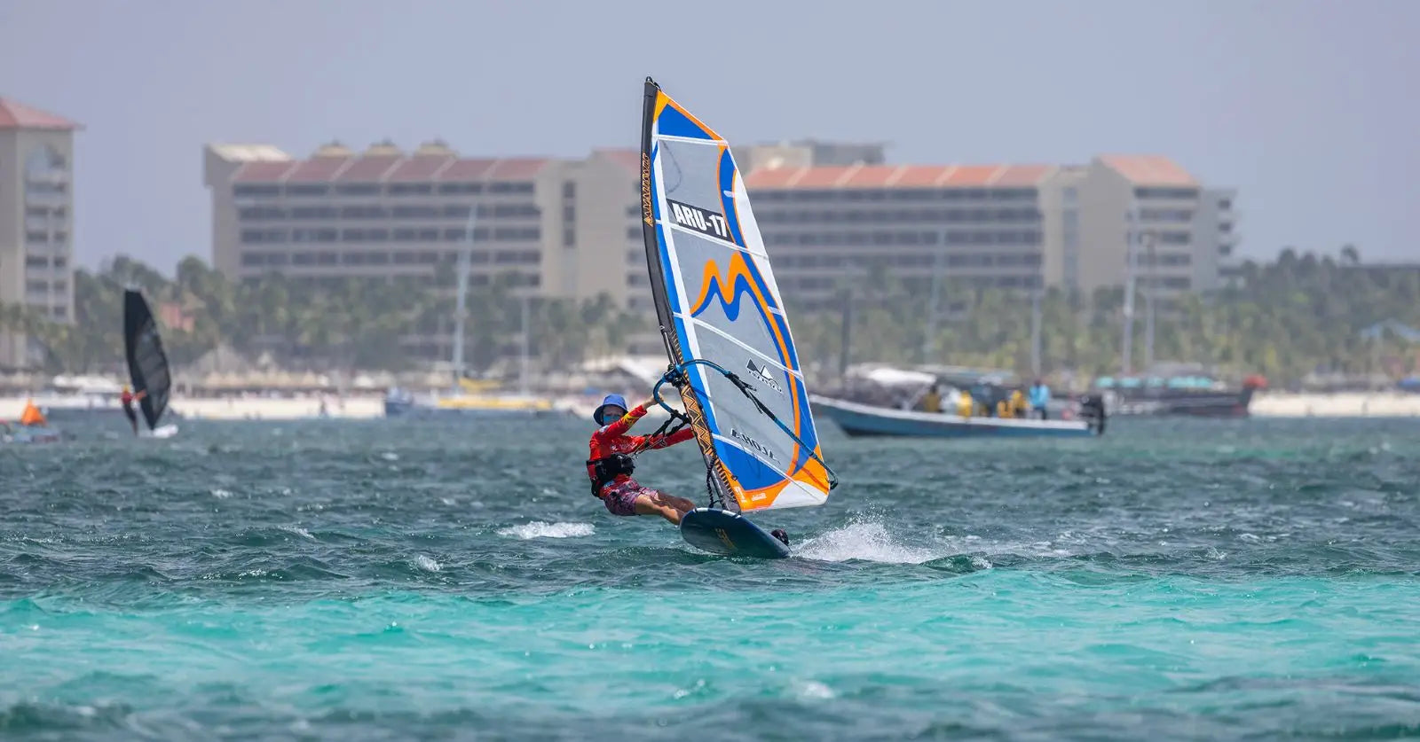 Windsurfing board with blue and white sail, red harness, black fins