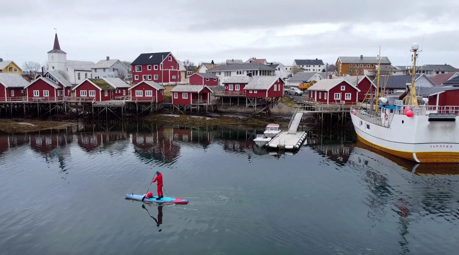 Red polyethylene foam stand-up paddleboard with black leash and white logo for Lofoten fjords.
