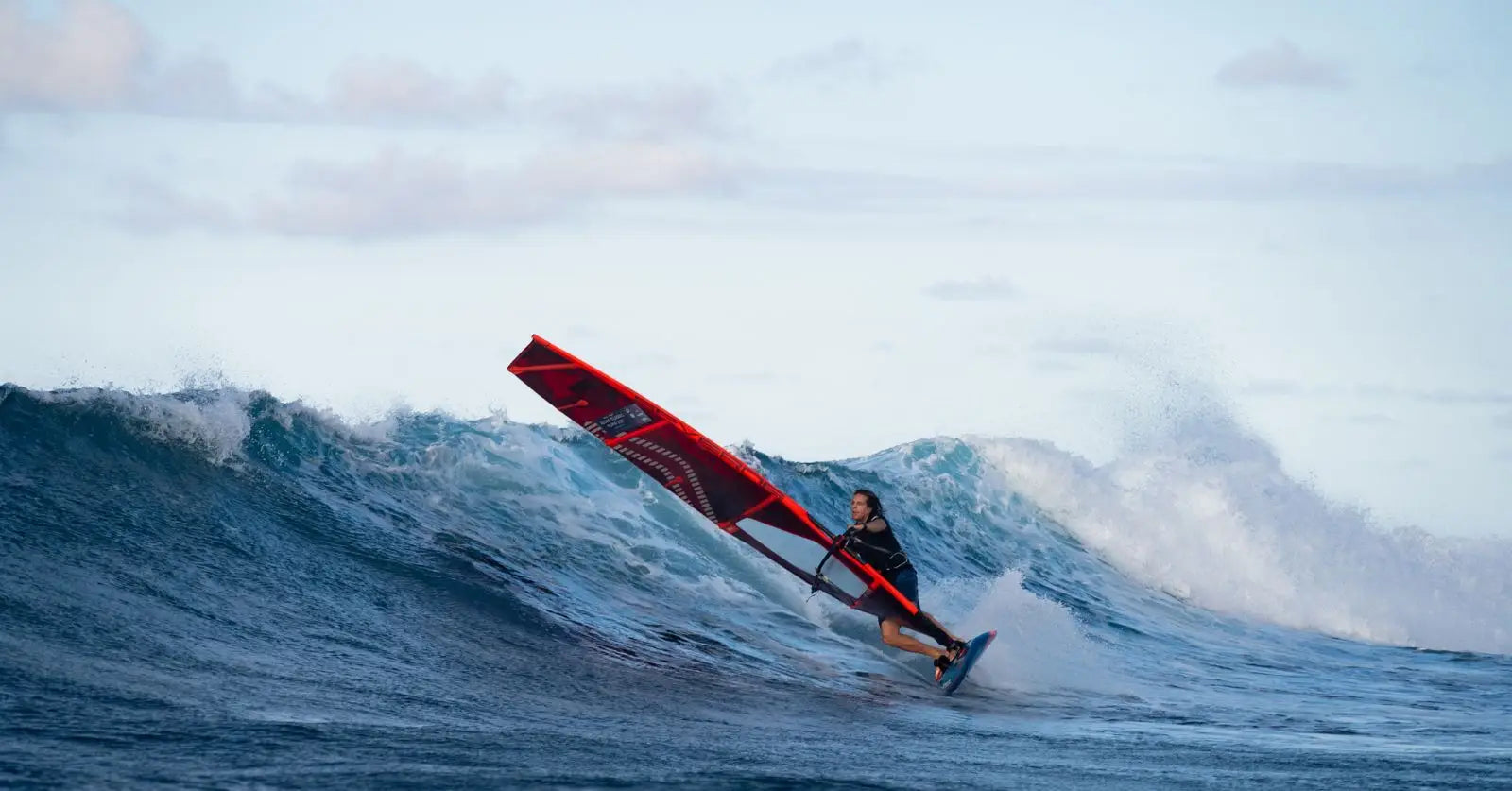 Red windsurfing board with black sail and white trim for high-performance sailing