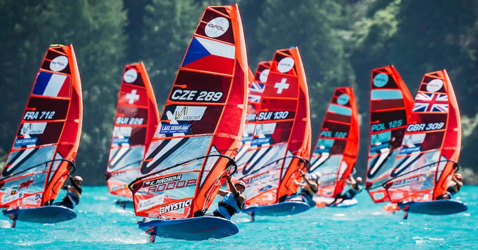 Red and white iQFOiL windsurfing board with orange sail and flags