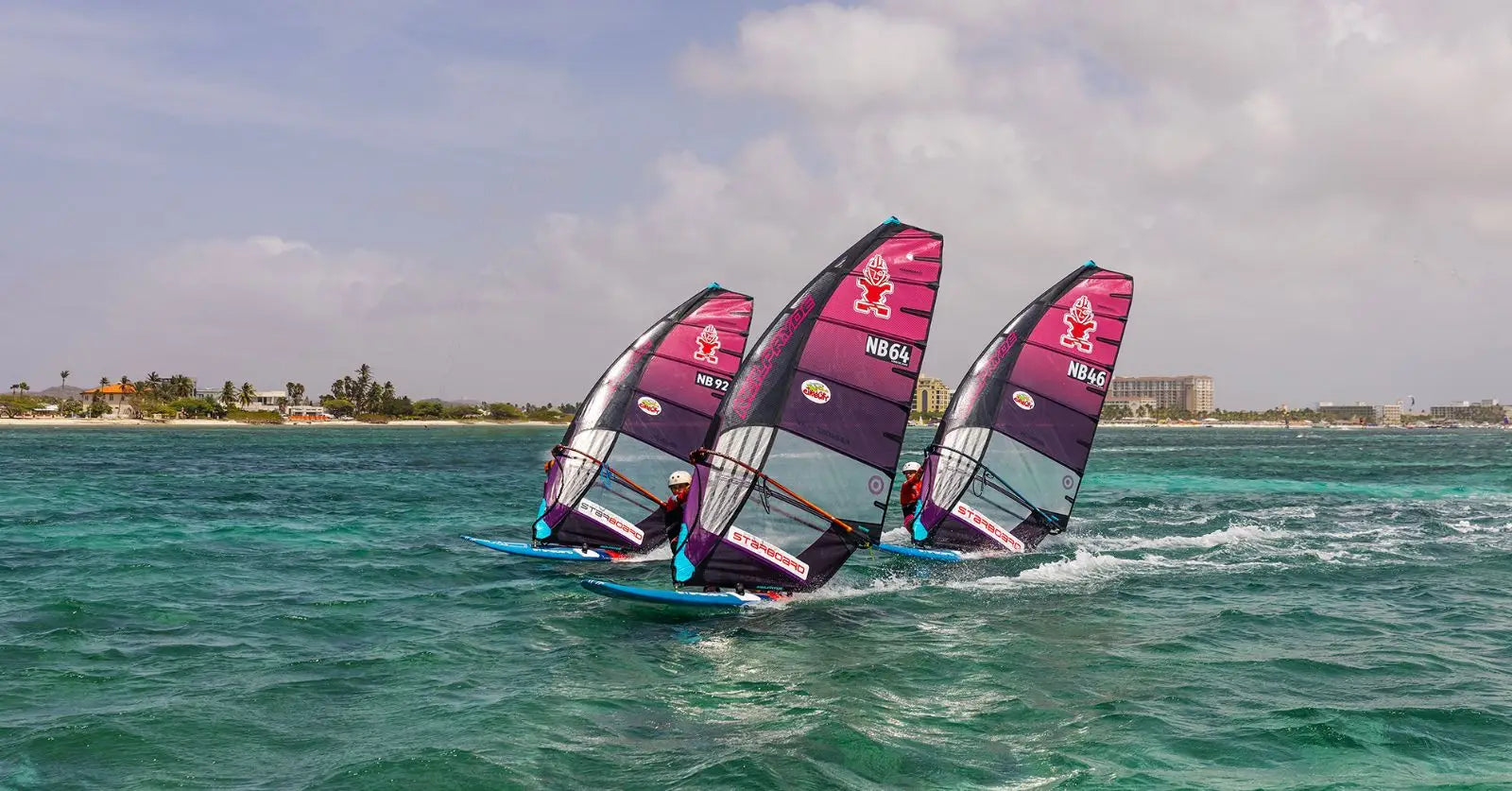 Nacra purple pink windsurfing sail with blue board at PWA Aruba Hi Winds