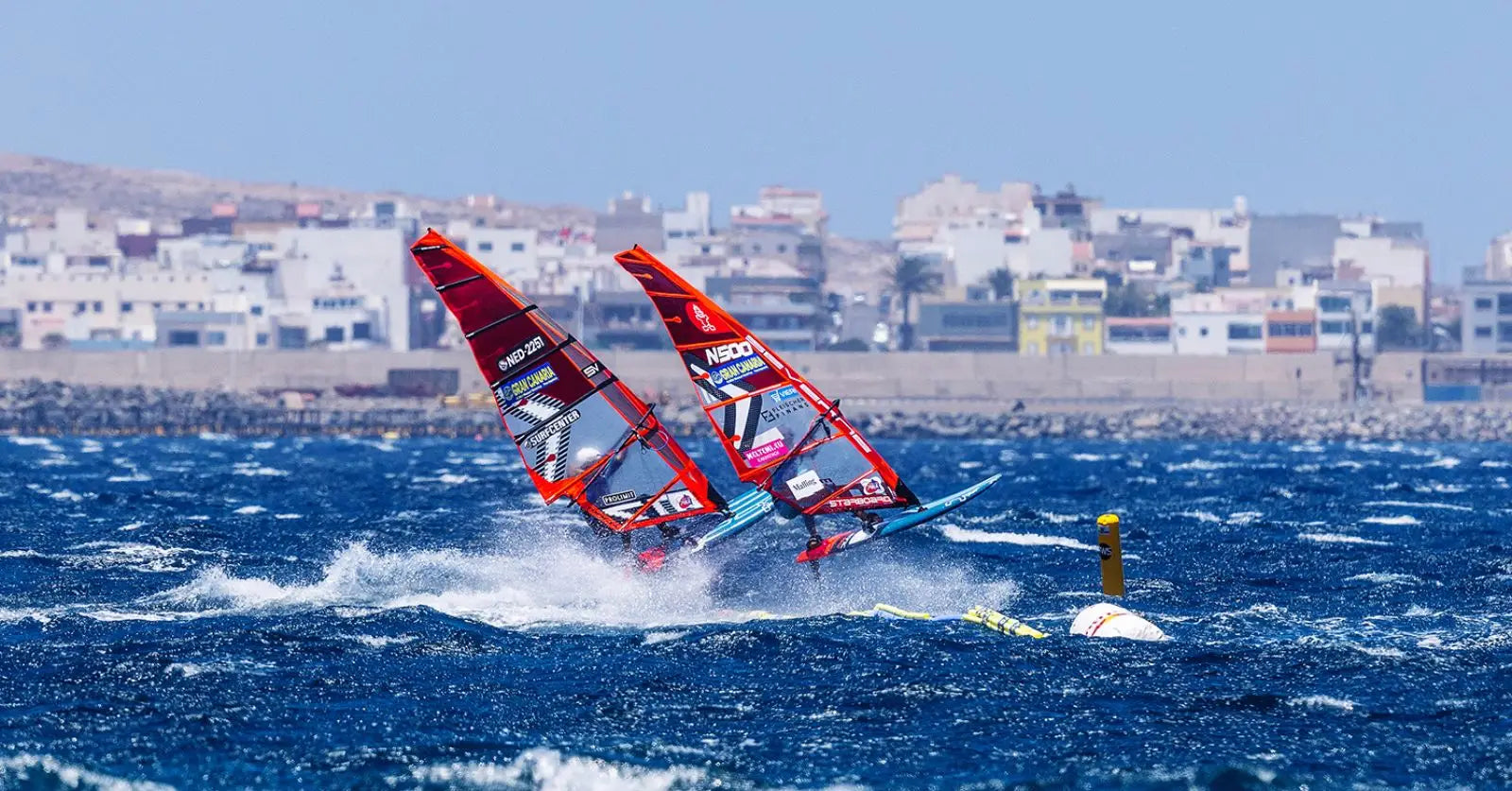 Red and white Starboard windsurfing board with North sail and blue fins