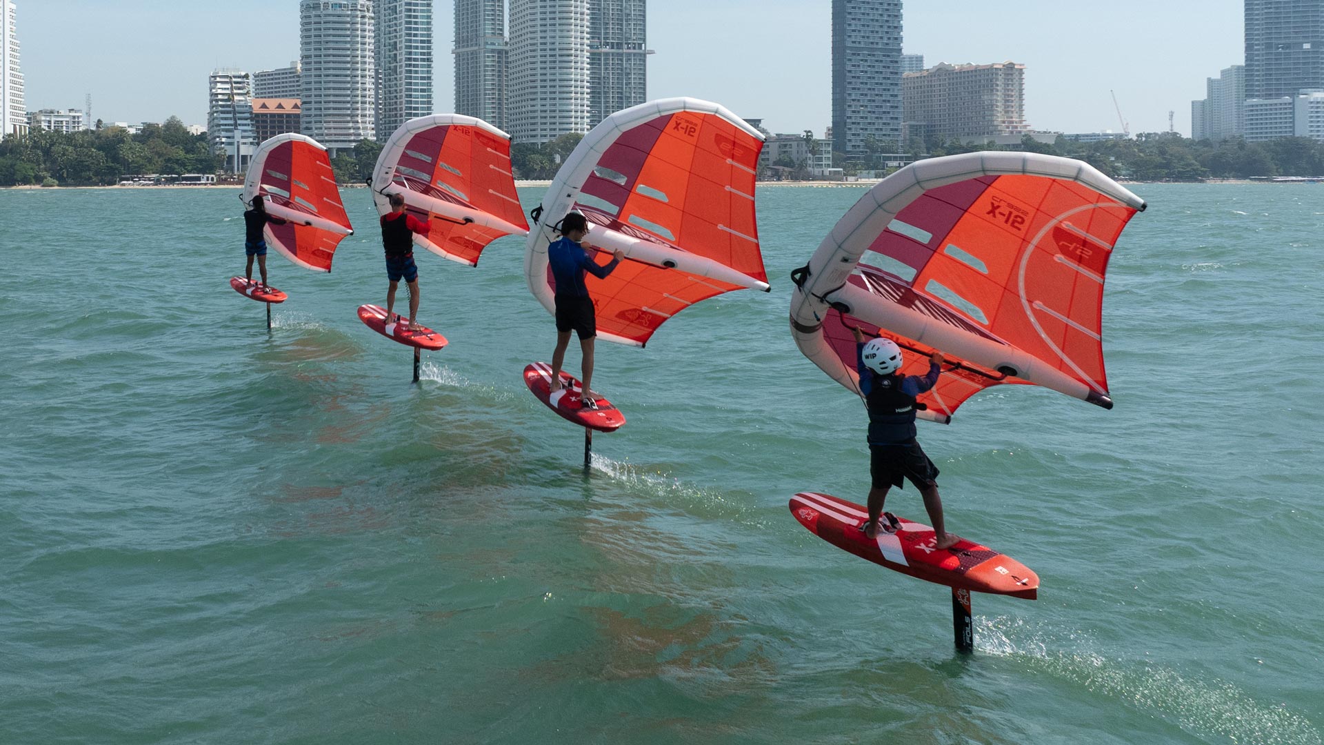 X-15 Foilboards windsurfing board with red white sail orange fins black harness blue water