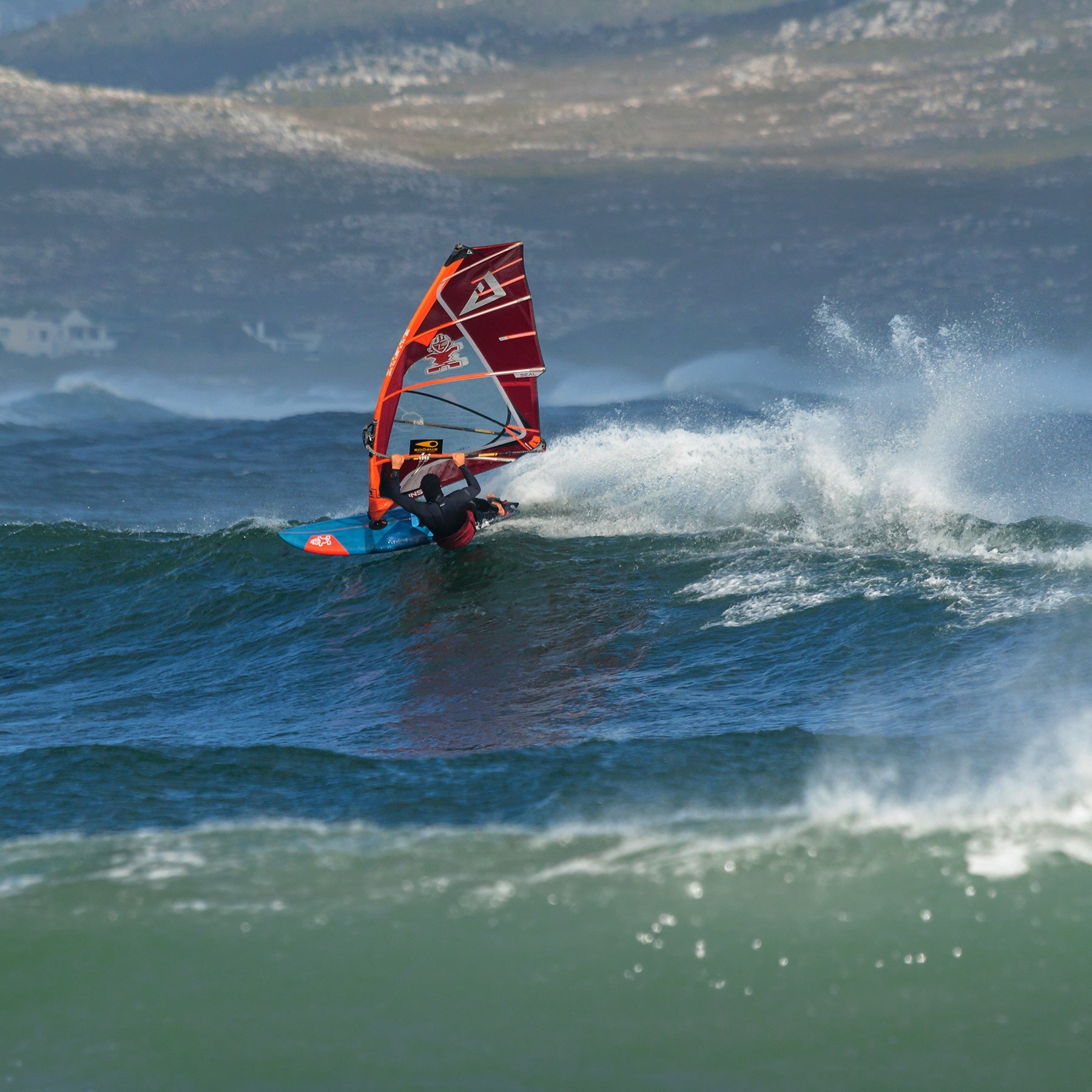 Blue and red windsurf board with white fins, fiberglass or foam