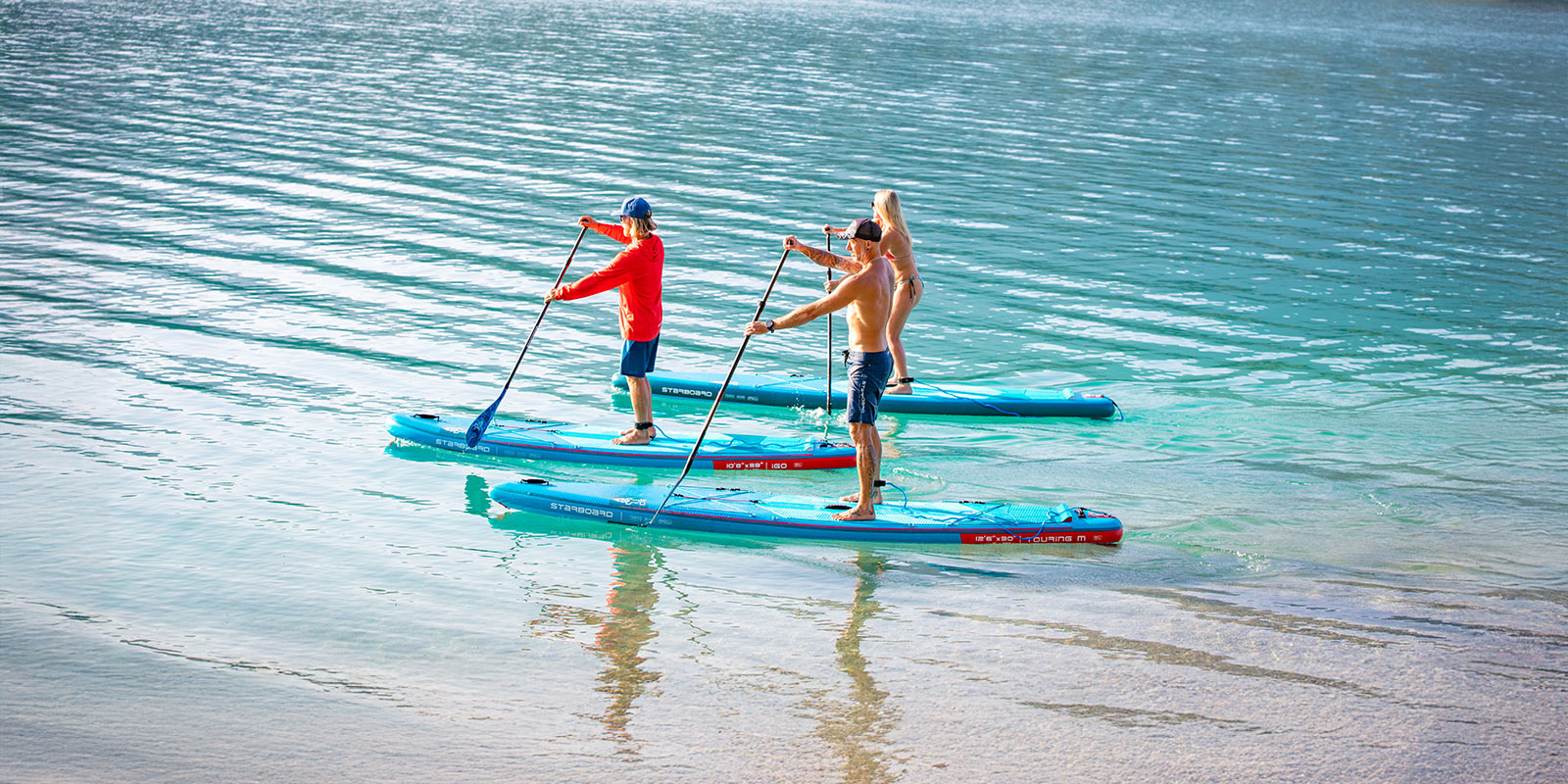 Group of seven paddlers standing on Starboard inflatable paddle boards on calm water with green mountains in the background